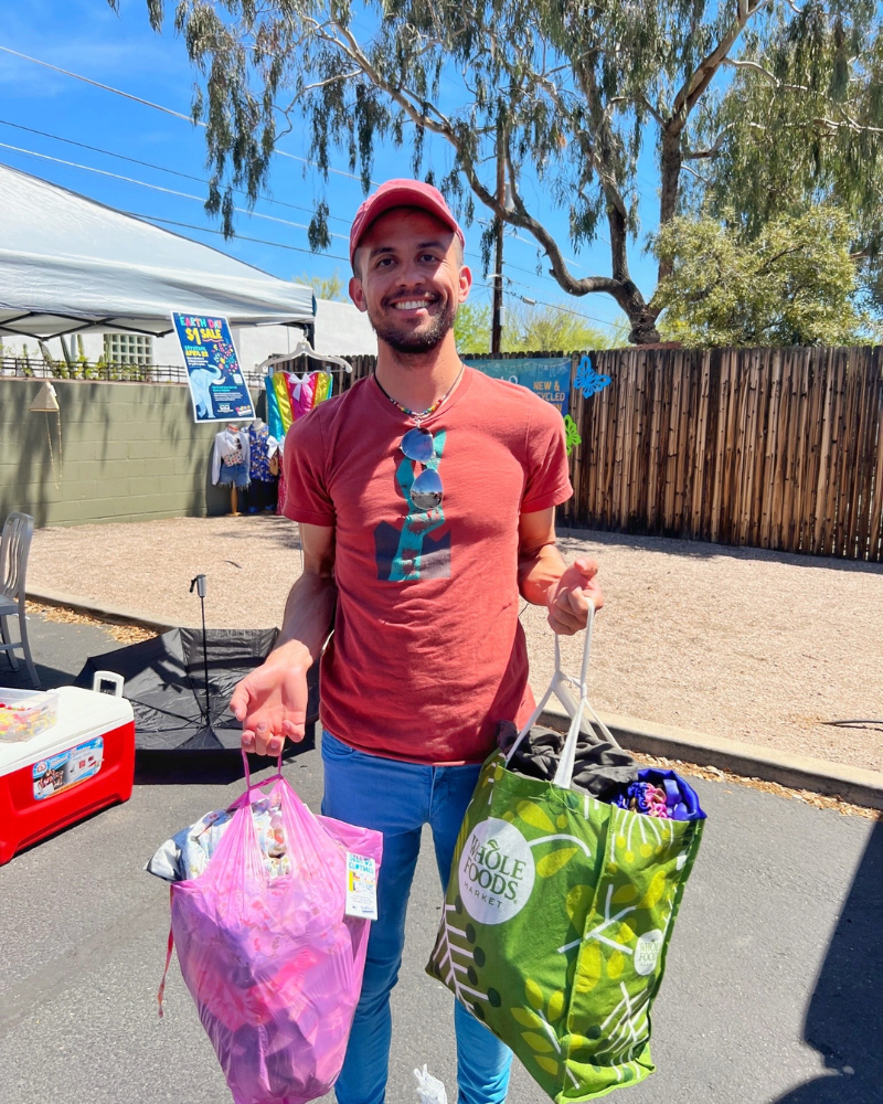 a man standing in a parking lot smiles while holding to bags full of clothing